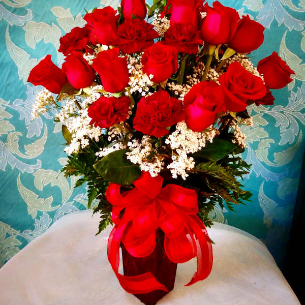 Red roses and carnations arranged in a vase with a red ribbon