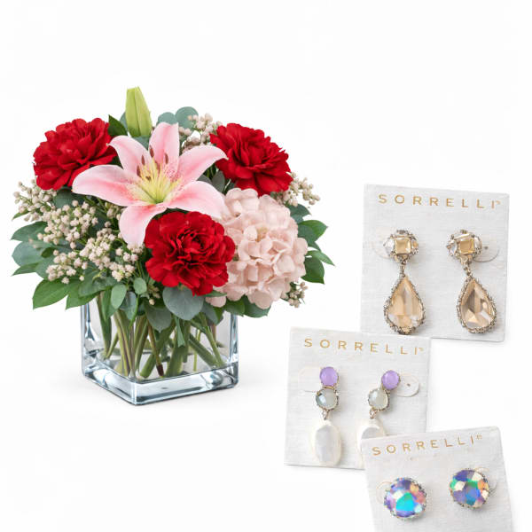 Bouquet of red and pink flowers in a square glass vase with three pairs of earrings beside it