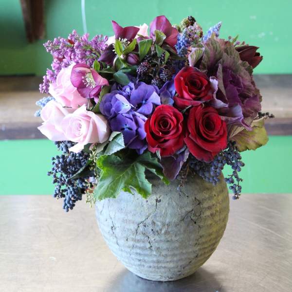 Mixed bouquet of roses, hydrangea, and purple blooms in a textured vase