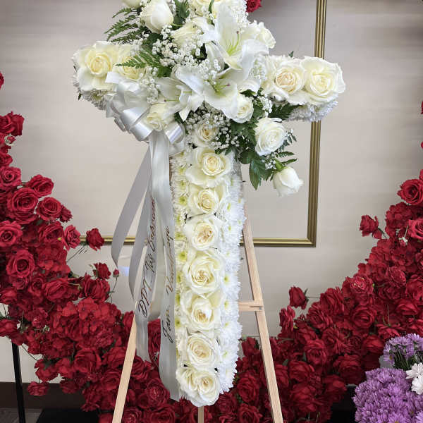 White floral cross arrangement on an easel with red rose backdrop