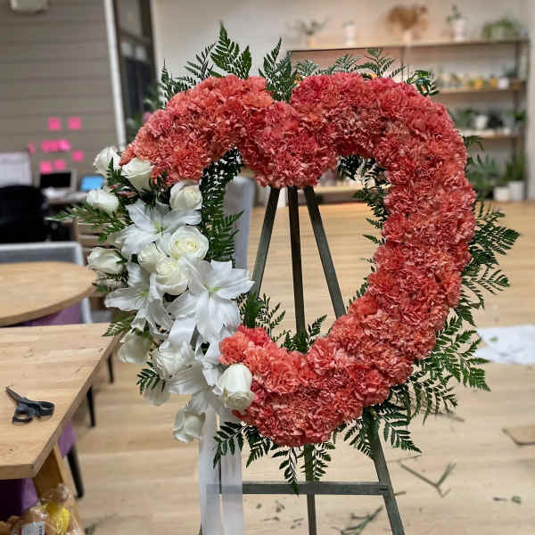 Heart-shaped floral wreath with pink carnations and white roses on an easel