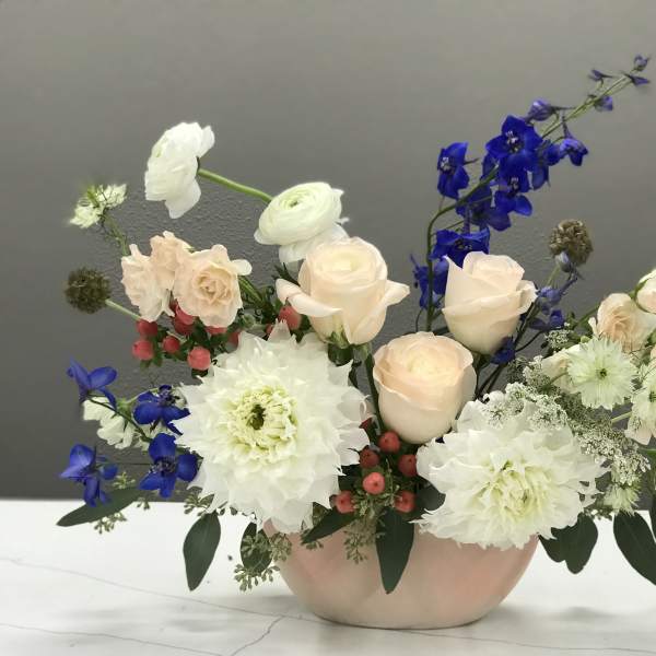Pastel floral arrangement in a low pink vase with white and blue blooms