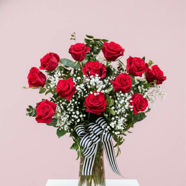 Red roses arranged in a clear glass vase with a striped ribbon