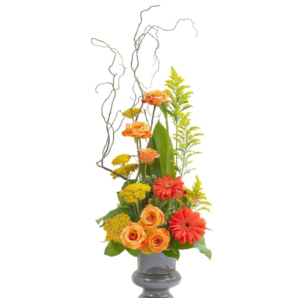 Tall arrangement of orange roses and gerbera daisies with yellow blooms in a gray vase