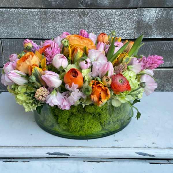 Mixed pink, orange, and lavender flowers in a low glass bowl