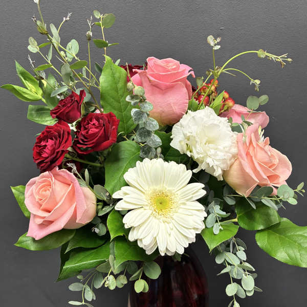 Mixed roses and a white gerbera daisy in a dark glass vase