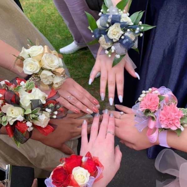 Hands wearing floral wrist corsages with roses and ribbons