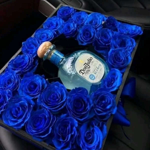 Blue roses arranged around a Don Julio tequila bottle in a gift box