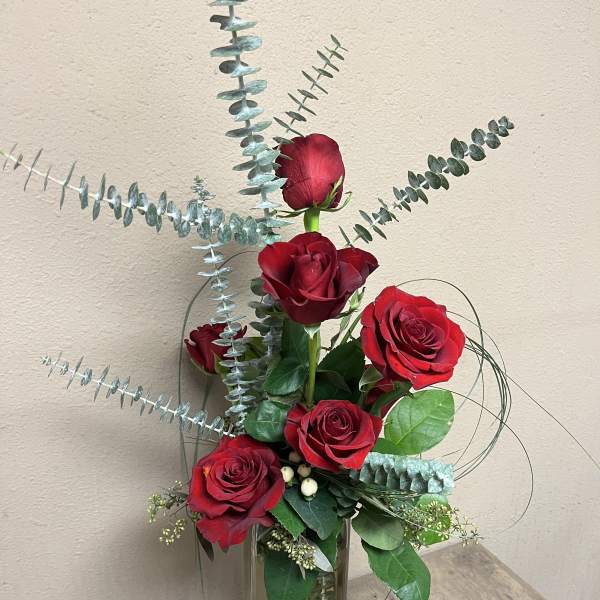 Red roses in a tall glass vase with eucalyptus stems