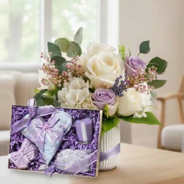 Bouquet of white and lavender roses in a striped vase with a purple gift box