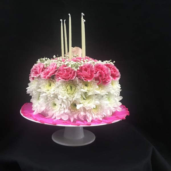 Pink and white floral cake with tall candles on a pedestal stand