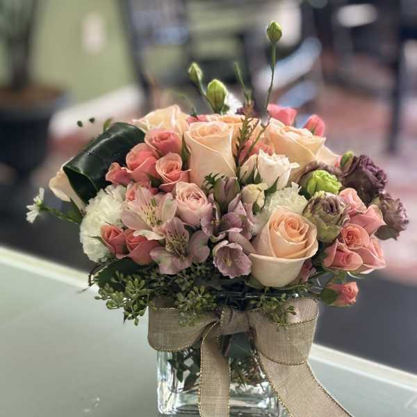 Pink and peach roses arranged in a glass vase with a burlap bow