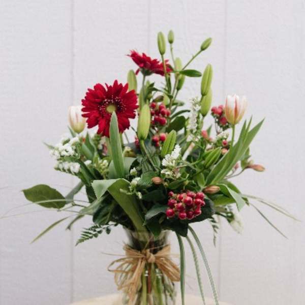 Tall bouquet of red and white flowers in a glass vase with a ribbon bow