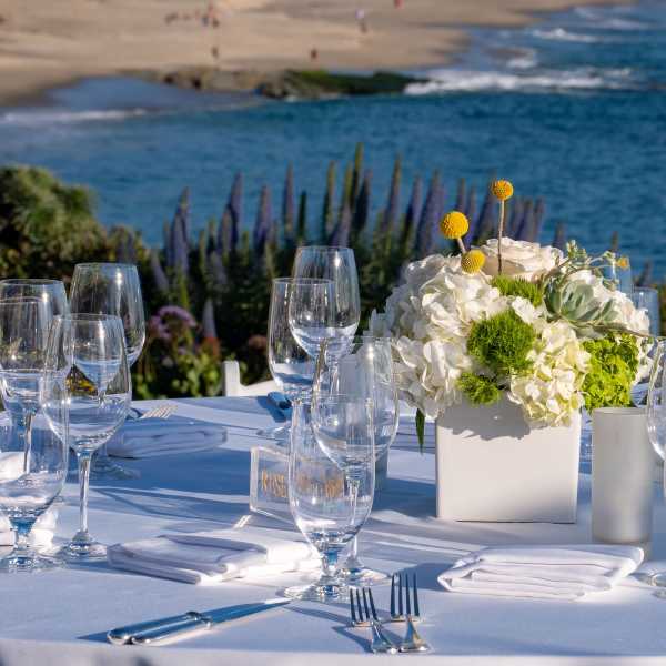 White floral centerpiece in a square vase on a set table by the water