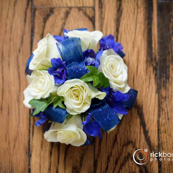 White roses with blue ribbon and purple flowers on a wooden surface
