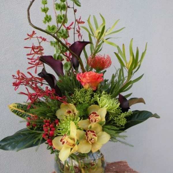 Tall tropical flower arrangement in a glass vase with orchids and calla lilies