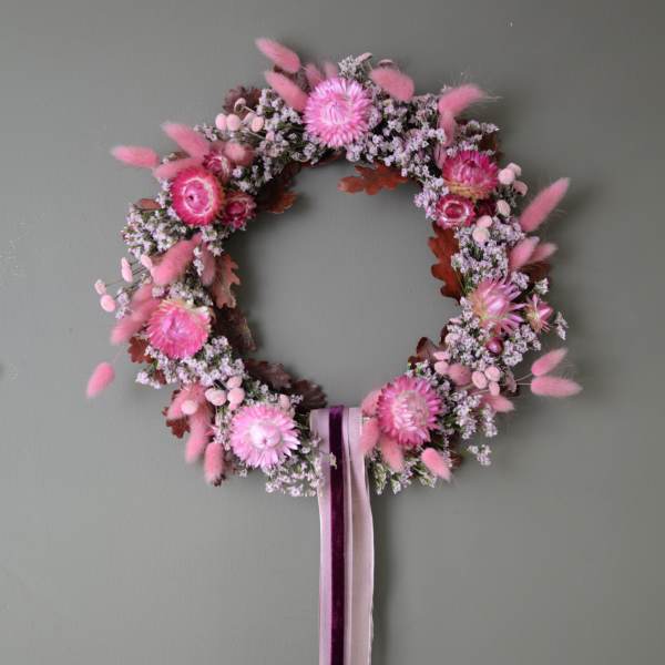 Pink floral wreath with ribbon tails on a gray wall