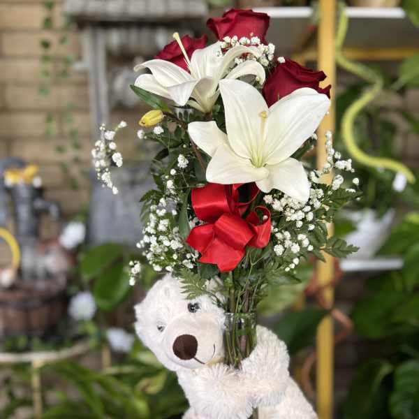 Bouquet of white lilies and red roses in a glass vase with a teddy bear