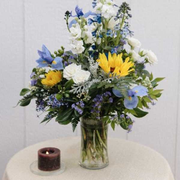 Blue and white floral arrangement in a glass vase with a candle beside it
