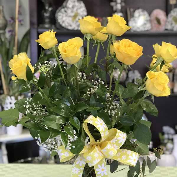 Yellow roses in a glass vase with a yellow daisy ribbon