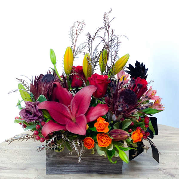 Mixed bouquet with pink lilies, red roses, and orange spray roses in a black box