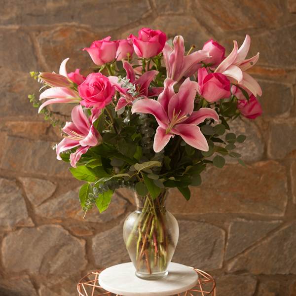 Pink roses and lilies arranged in a clear glass vase