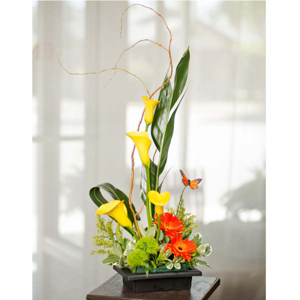 Tall floral arrangement with yellow calla lilies and orange gerbera daisies in a black container