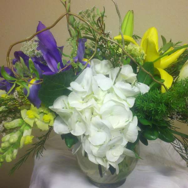 Bouquet of white hydrangea, purple iris, and yellow lilies in a glass vase