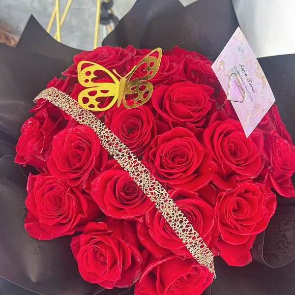 Bouquet of red roses wrapped in black paper with a gold butterfly decoration