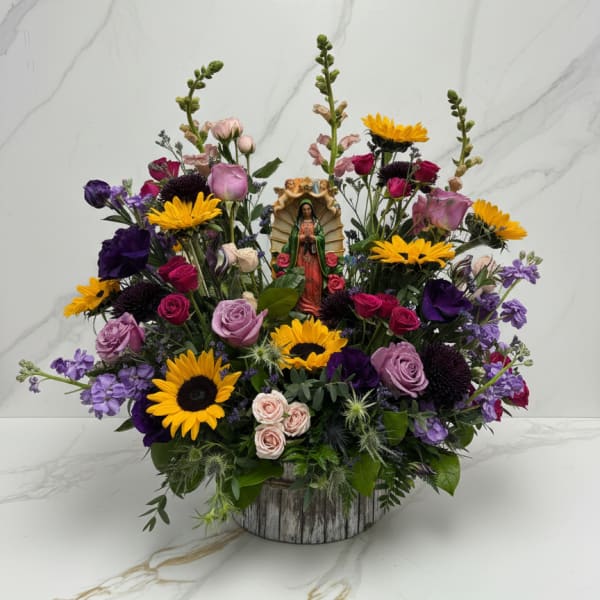 Colorful mixed flower arrangement with a small religious figurine in a rustic container