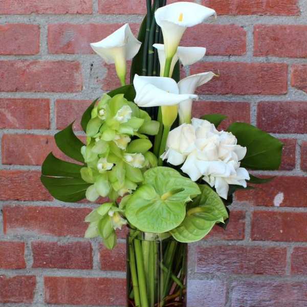 White calla lilies and green orchids in a tall glass vase