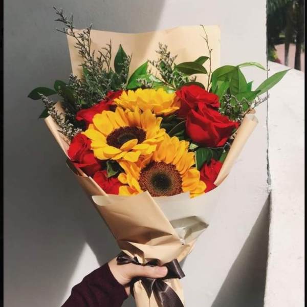 Bouquet of red roses and yellow sunflowers wrapped in beige paper