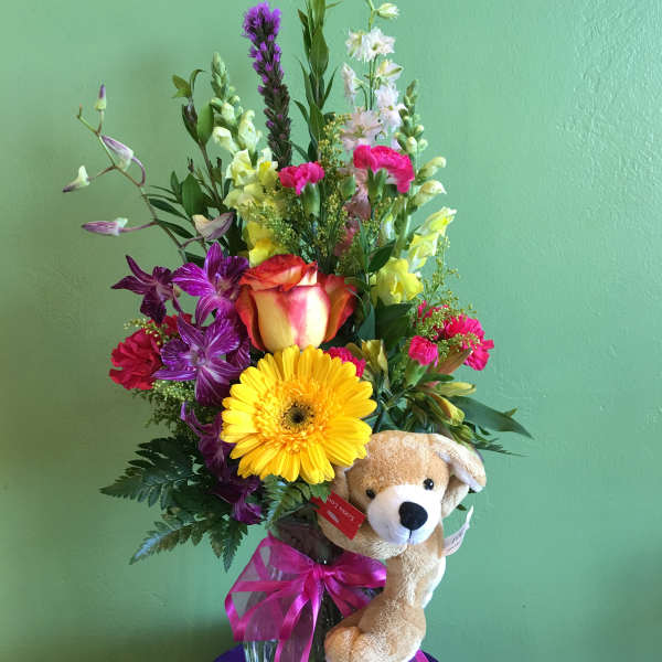 Mixed bouquet in a glass vase with a plush teddy bear and pink ribbon