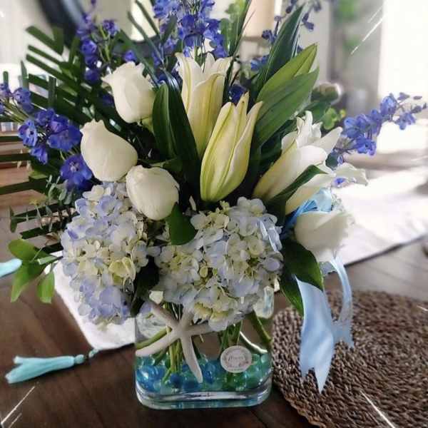 White tulips and blue flowers in a glass vase with blue beads