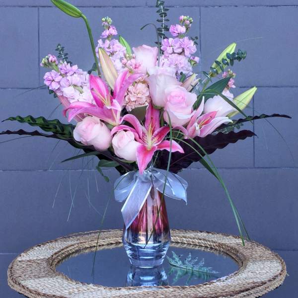 Pink lilies and roses arranged in a glass vase with a ribbon