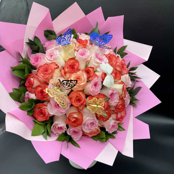 Round bouquet of pink and coral roses with butterfly accents wrapped in pink paper