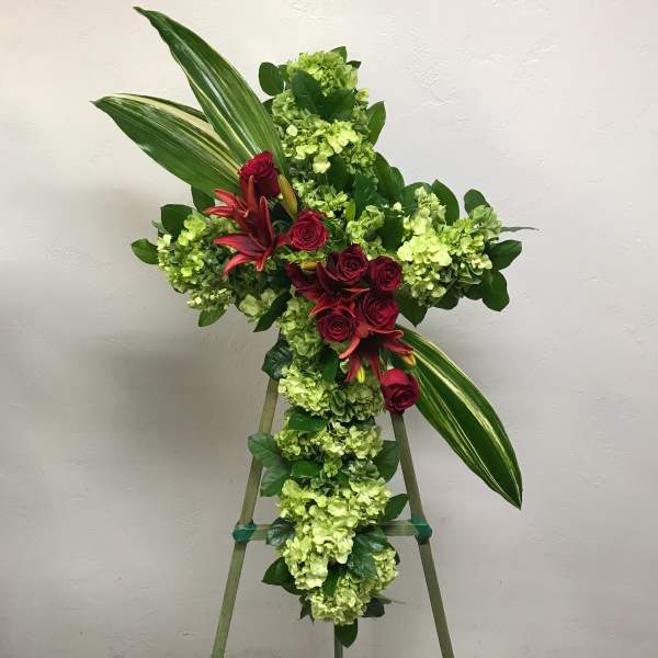 Cross-shaped floral spray with red roses and green hydrangeas on an easel