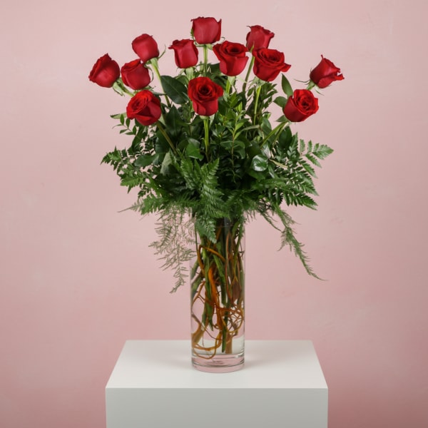 Tall vase of red roses with greenery on a white pedestal