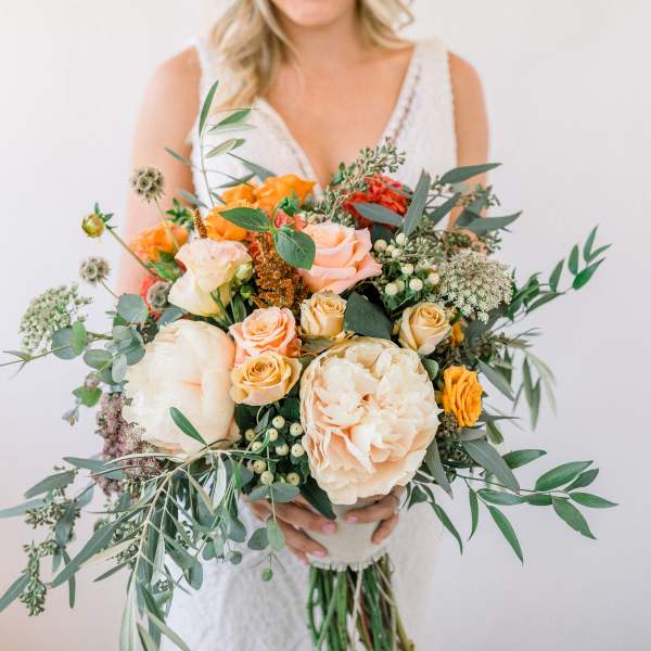 Bride holding a bouquet of peach and orange roses with greenery