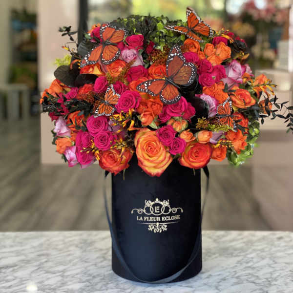 Bouquet of orange and pink roses in a black hat box with butterfly decorations