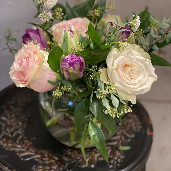 Bouquet of pale pink and cream roses with purple tulips in a glass vase