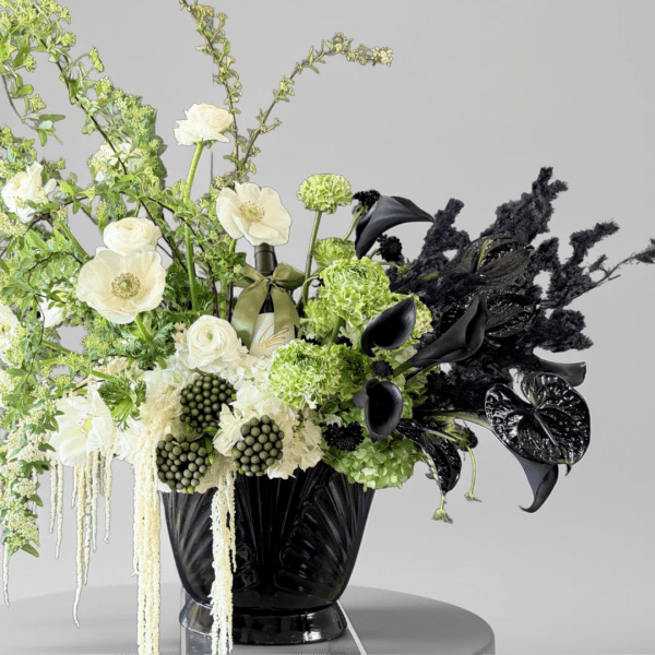 Black vase with white and green floral arrangement and black calla lilies