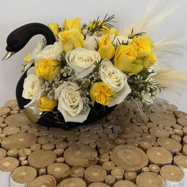 Yellow and white rose arrangement in a black swan-shaped container