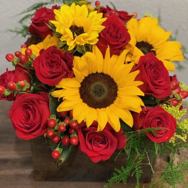 Bouquet of red roses and yellow sunflowers in a square vase