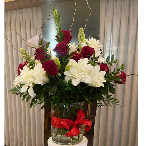 Tall arrangement of red roses and white lilies in a clear glass vase with a red bow