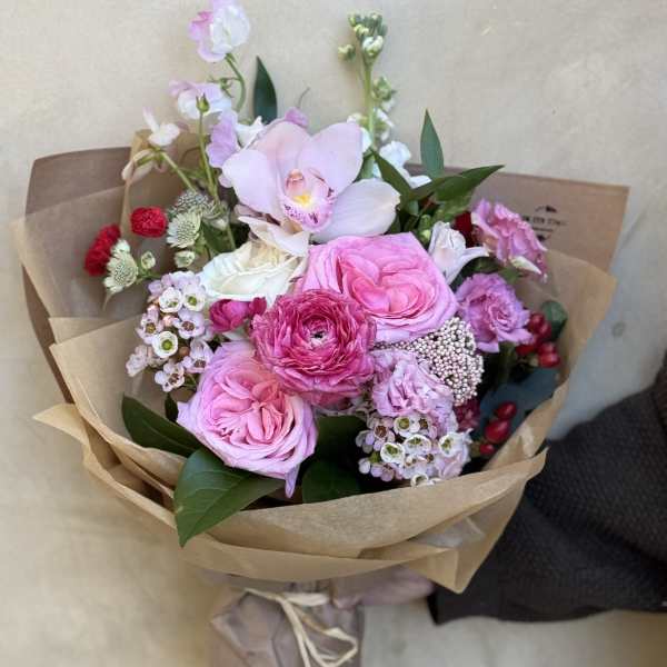 Pink and white bouquet with roses and orchids wrapped in brown paper