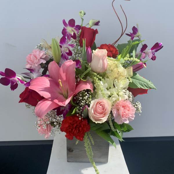 Mixed bouquet with pink lilies, roses, orchids, and carnations in a square vase