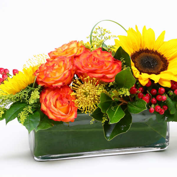 Sunflower and orange rose arrangement in a rectangular glass vase