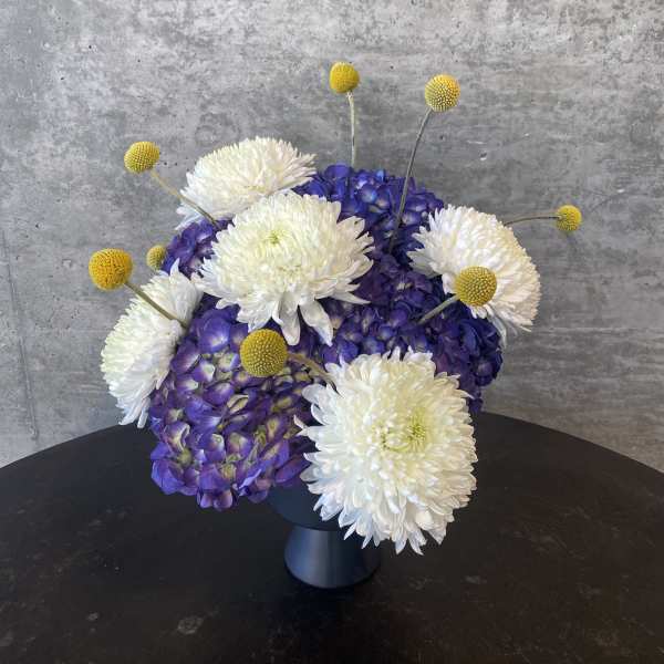 White chrysanthemums and purple hydrangeas in a dark vase with yellow button accents