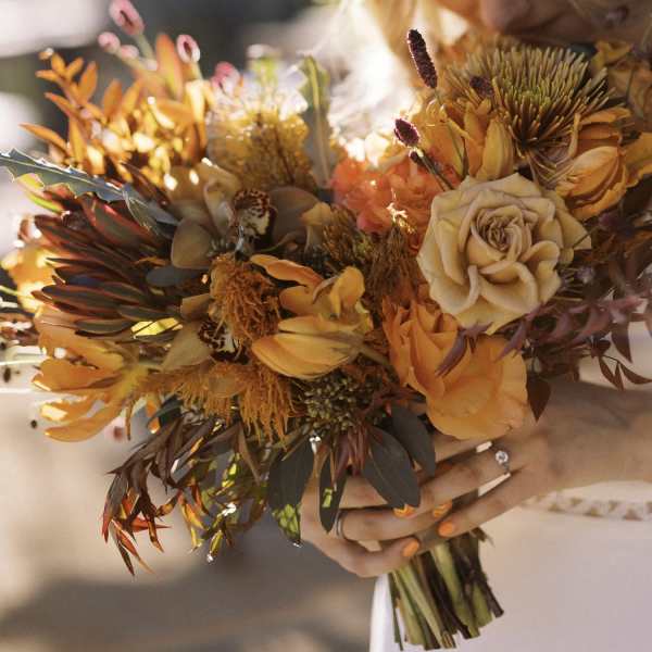 Handheld bouquet of orange and cream flowers with dark foliage